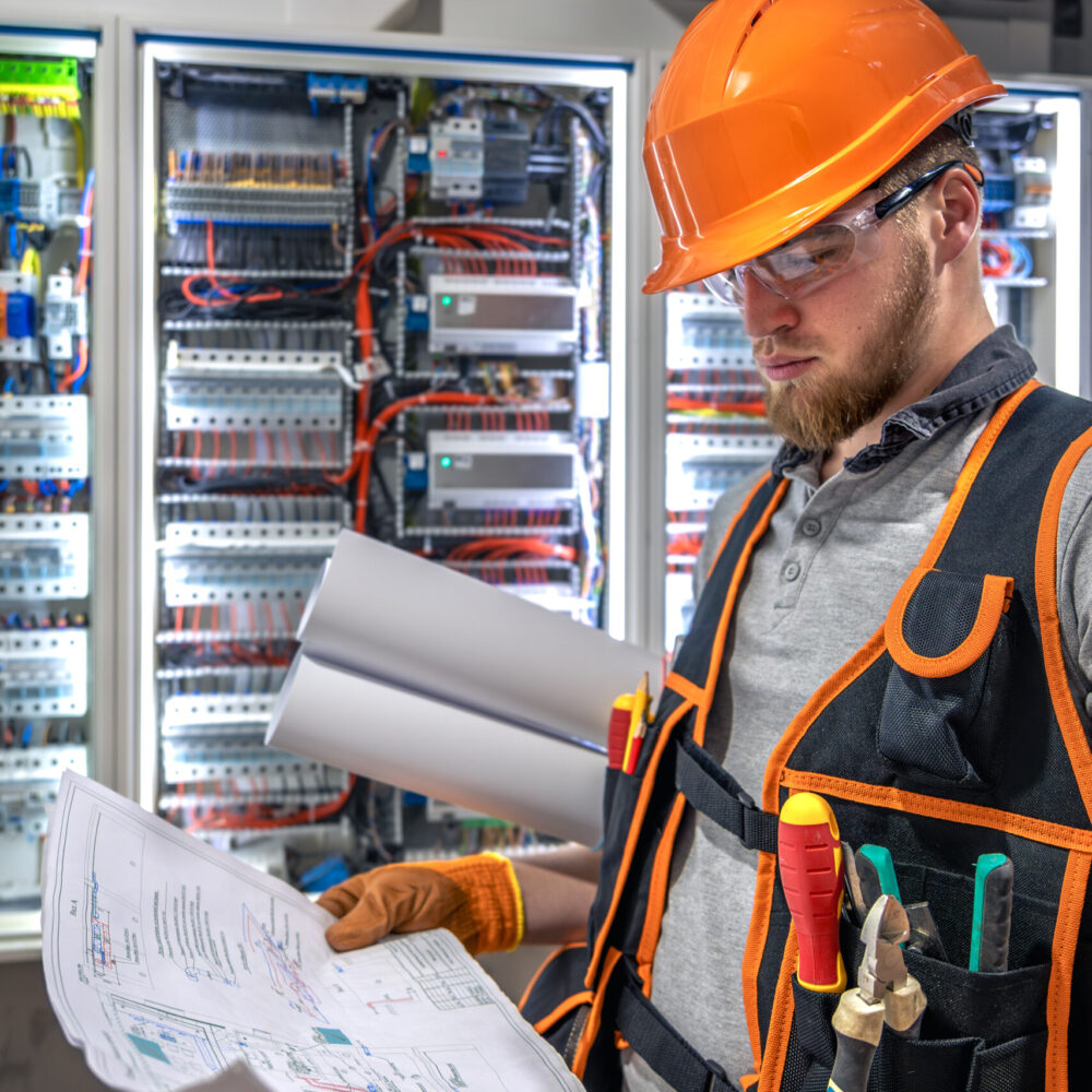 Male electrician working in electrical panel. Male electrician in uniform. High quality photo. Male construction worker in helmet and safety glasses.